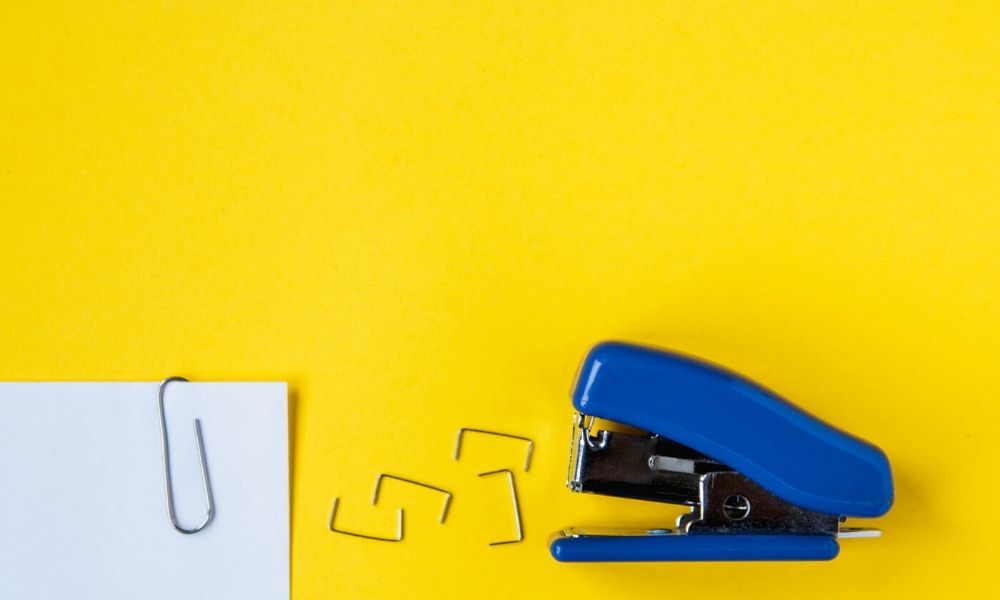 A stapler, staples, and a document with a paper clip with a yellow background.