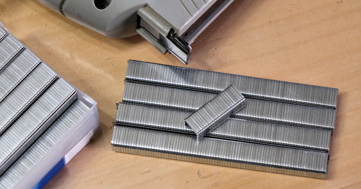 Several stacks of staples lie next to each other on a table next to a gray staple gun. A package of staples sits to the left.