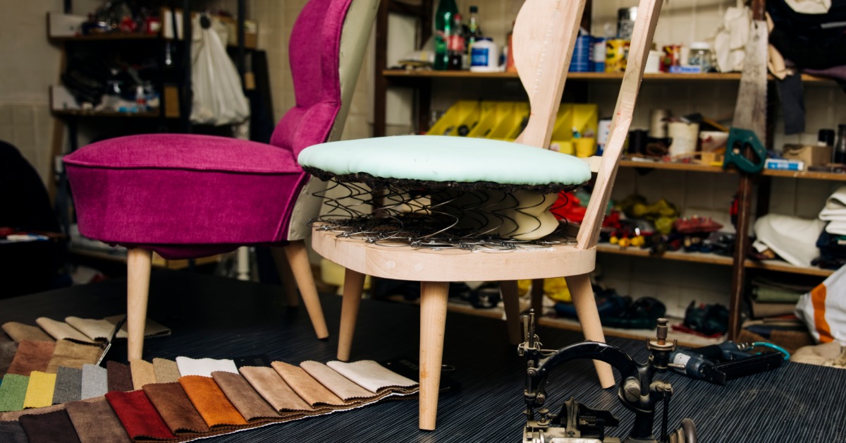 Two chairs, fabric swatches, tools, and supplies arranged on a worktable inside an upholstery workshop.